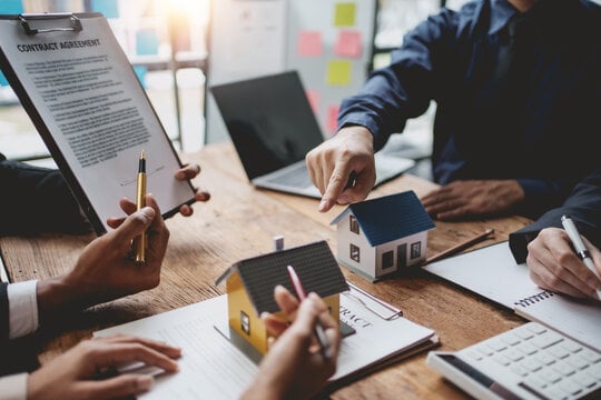 Hands of business people pointing at small house models on table with clipboard contract and laptop, signing signed!